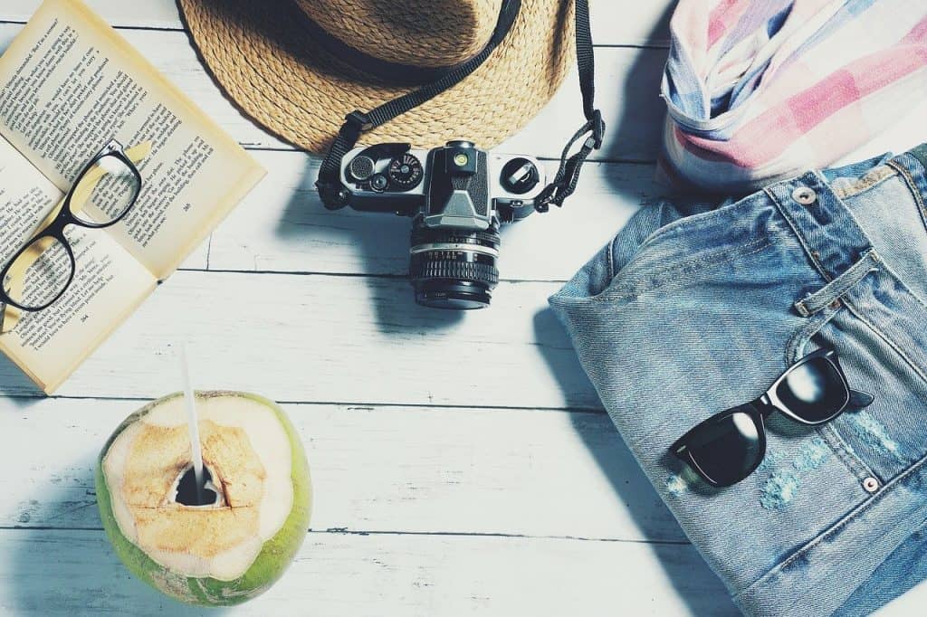 Collection of things to do when you can't travel - camera, book, sunglasses and clothes, and coconut drink