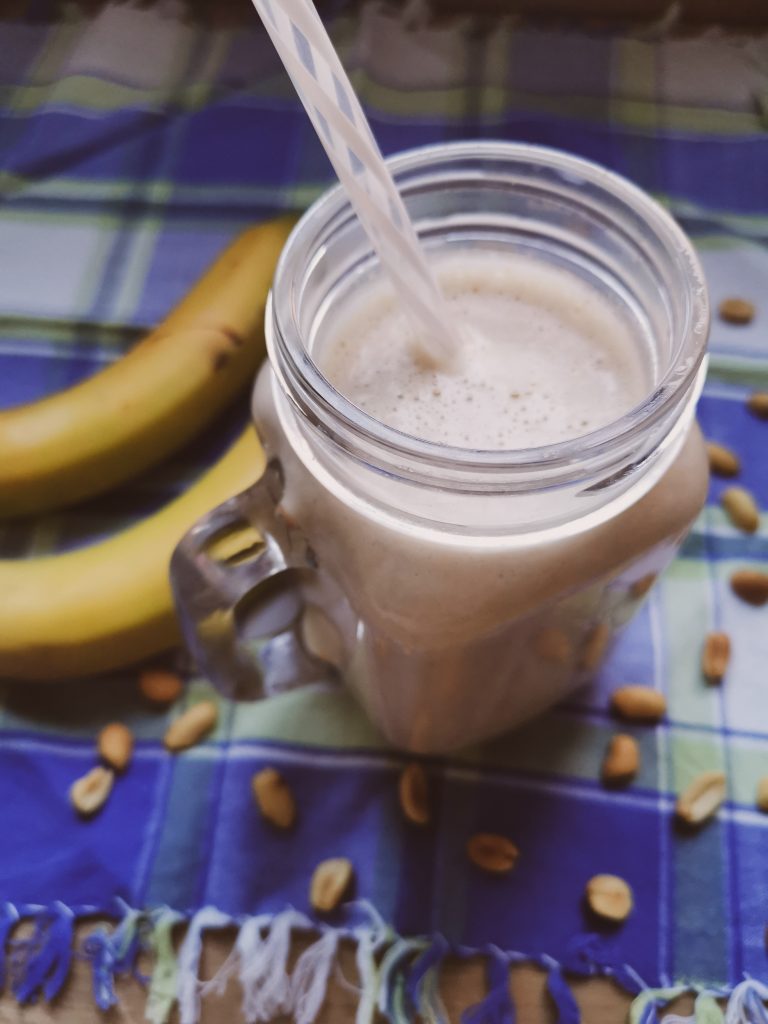 Smoothie in open jar with straw on picnic blanket with bananas and peanuts