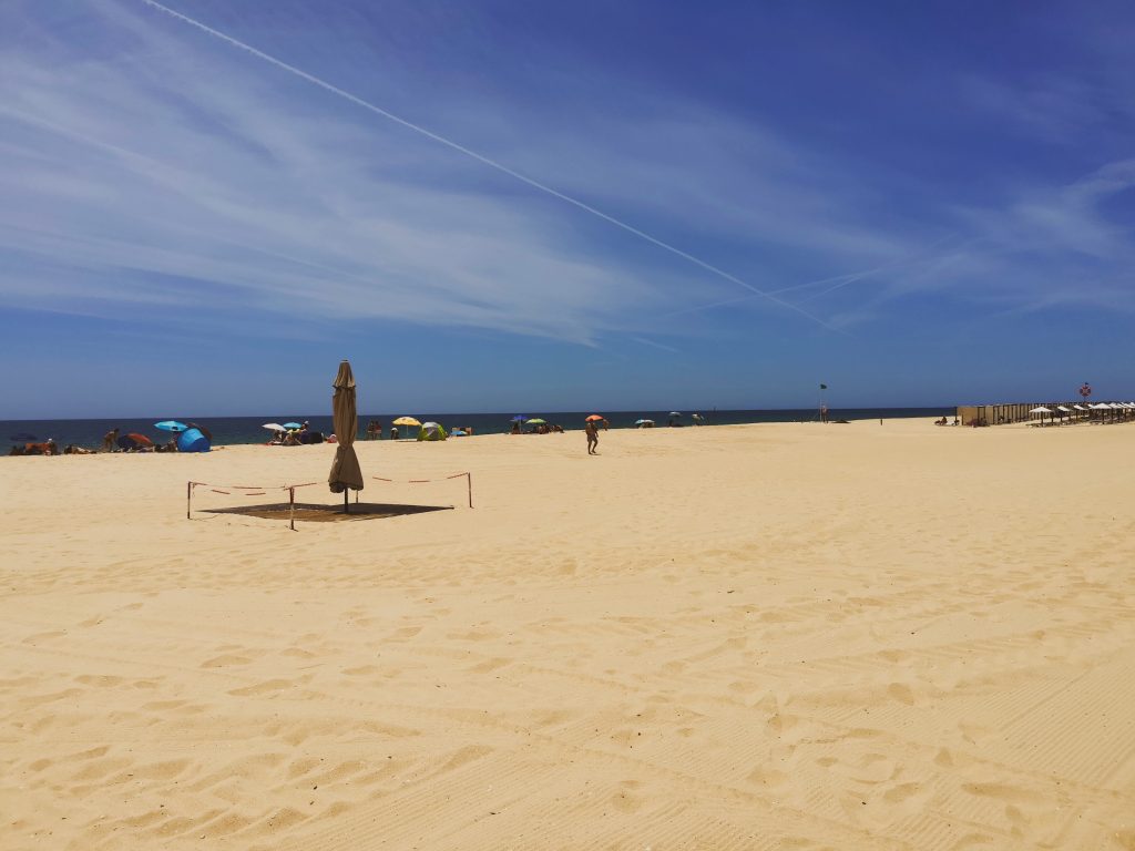 View of the white sands and blue sea at Tavira Island with beachgoers in the background under parasols