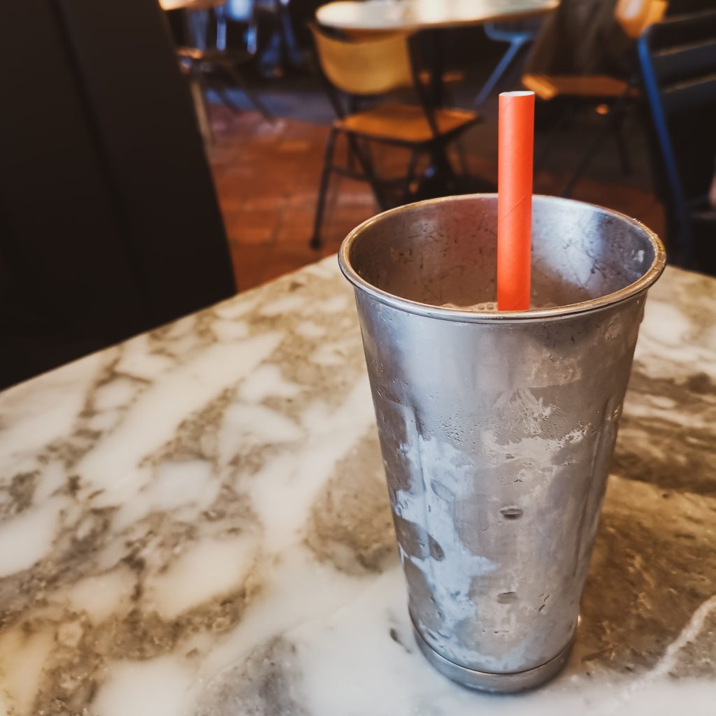 Metal milkshake container on marble-effect table with red straw