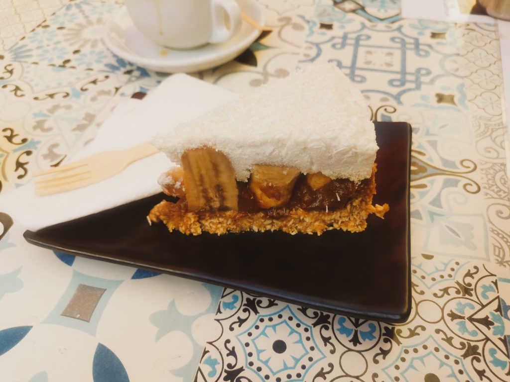 Example of vegan food in Malta - shot of banoffee cheesecake on a black plate with a wooden fork and white napkin
