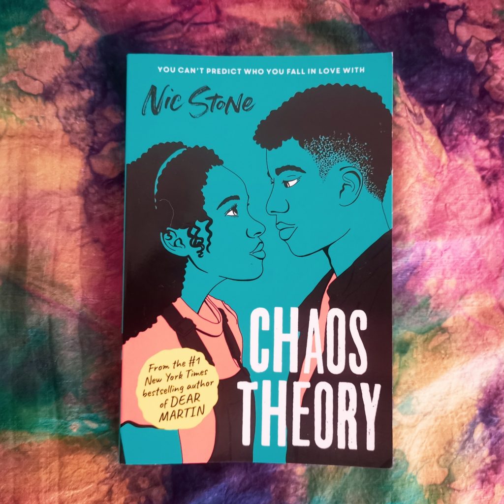 Aerial view of Chaos Theory by Nic Stone with blue cover and two teenagers looking into each others' eyes featuring multi-coloured material background similar to oil slick 