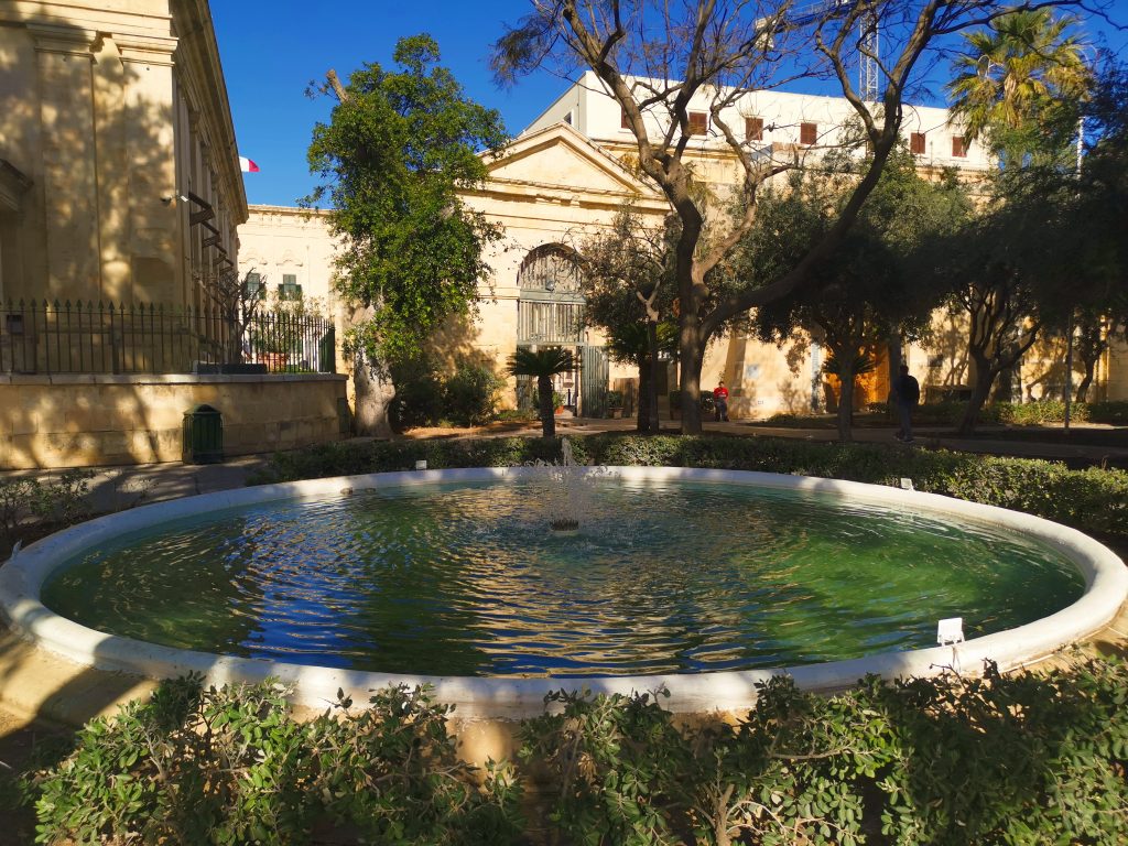 Large water fountain with green water in Lower Barrakka Garden surrounded by trees